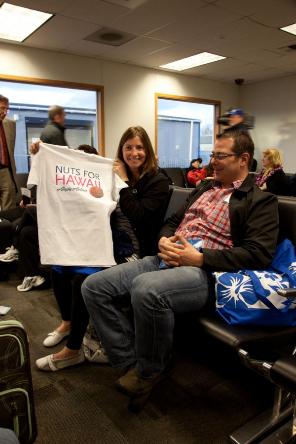Jordana Collison proudly displays her new shirt that was included in the gift bag provided to commemorate Alaska Airlines\' inaugural Bellingham to Honolulu flight. Jordana and her companion Chris Maslovich (right) traveled across the border from British Columbia for the flight. When asked how convenient the trip was for them,  Jordana remarked,